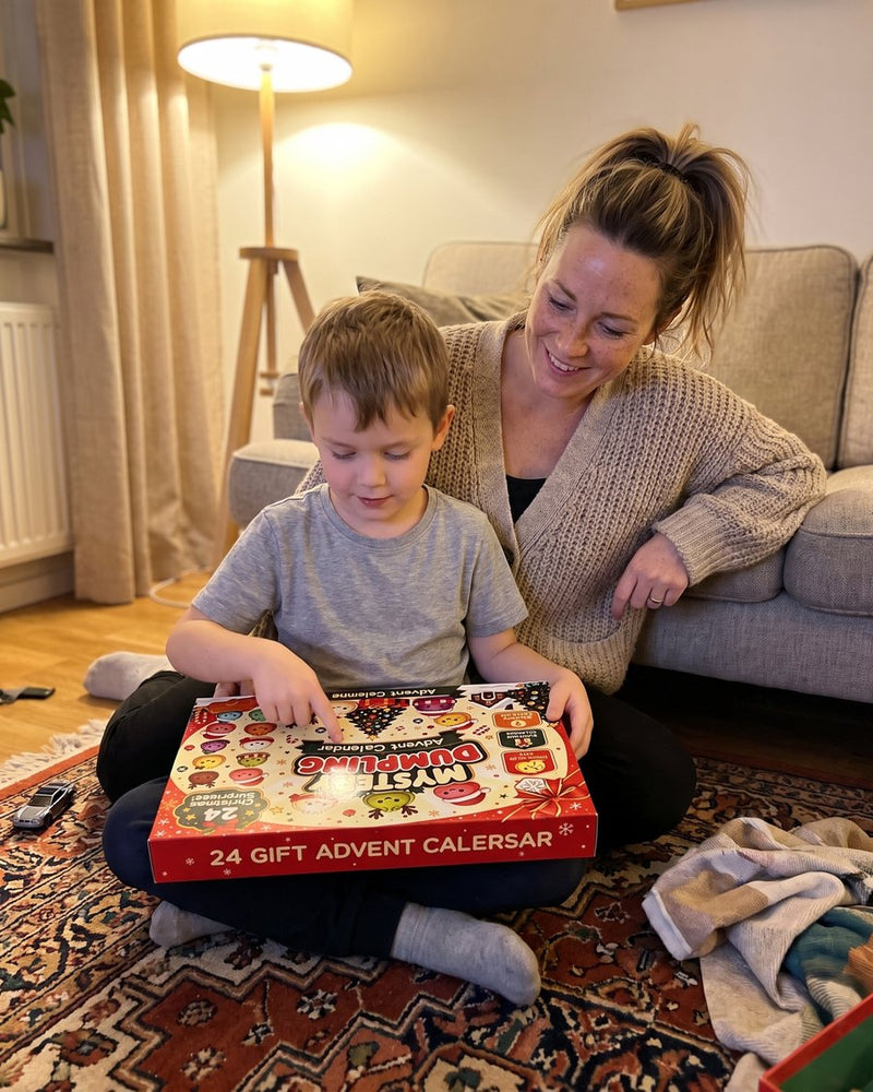 Pojke sitter på mattan med Dumplingkalendern i knät medan hans mamma tittar på honom och ler